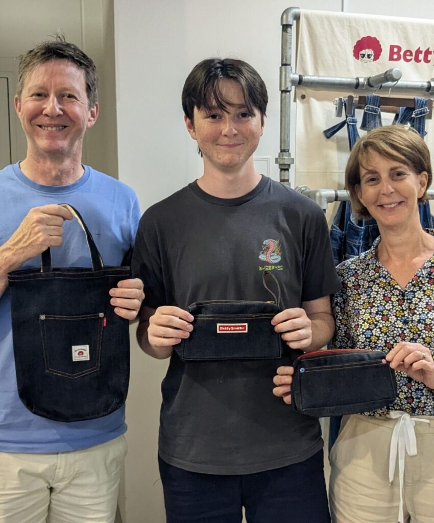 Parents and their child proudly showing their custom-made denim accessories inside a traditional Kojima textile studio.